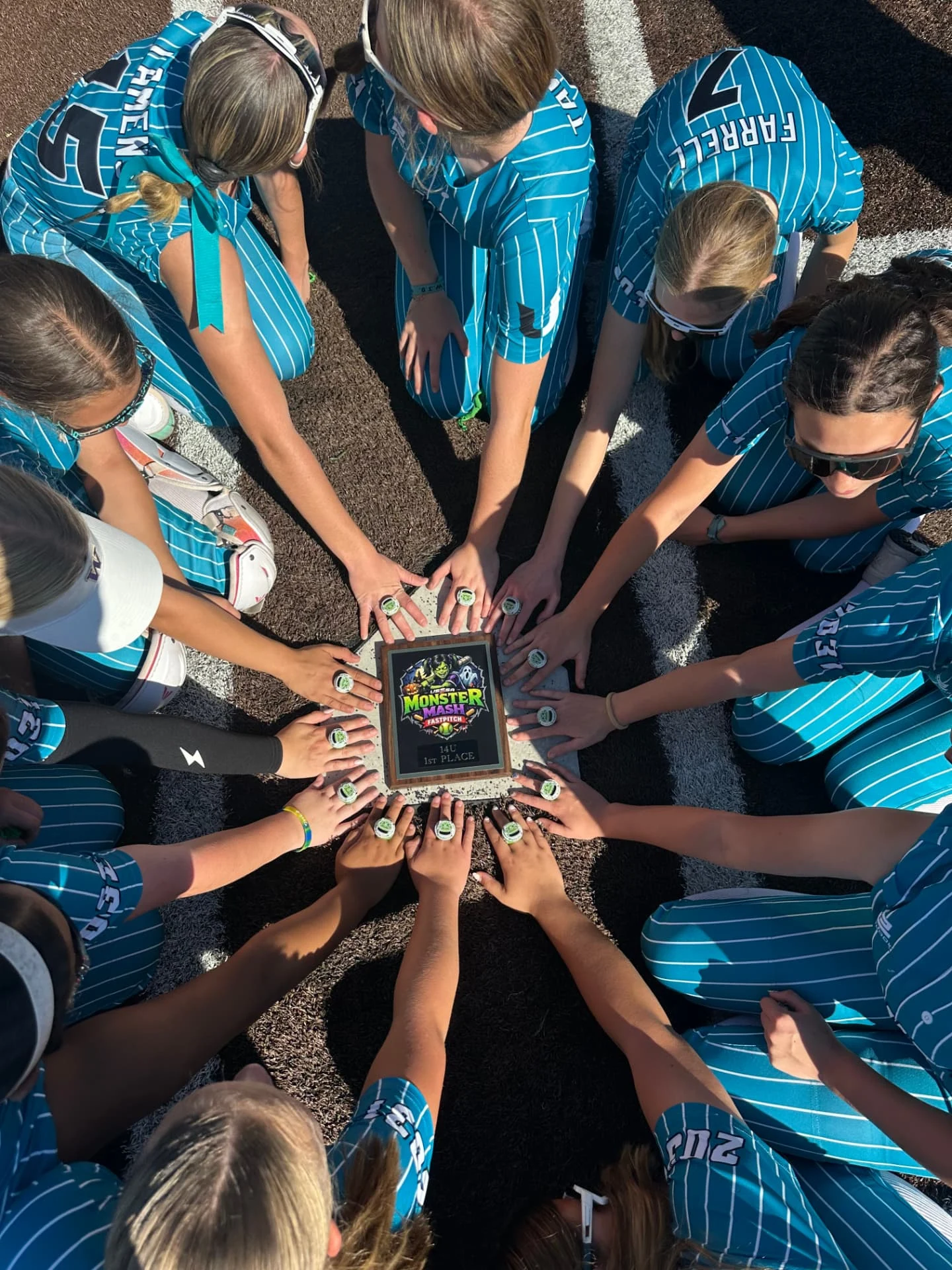 United Softball teammates displaying championship rings around a tournament trophy.
